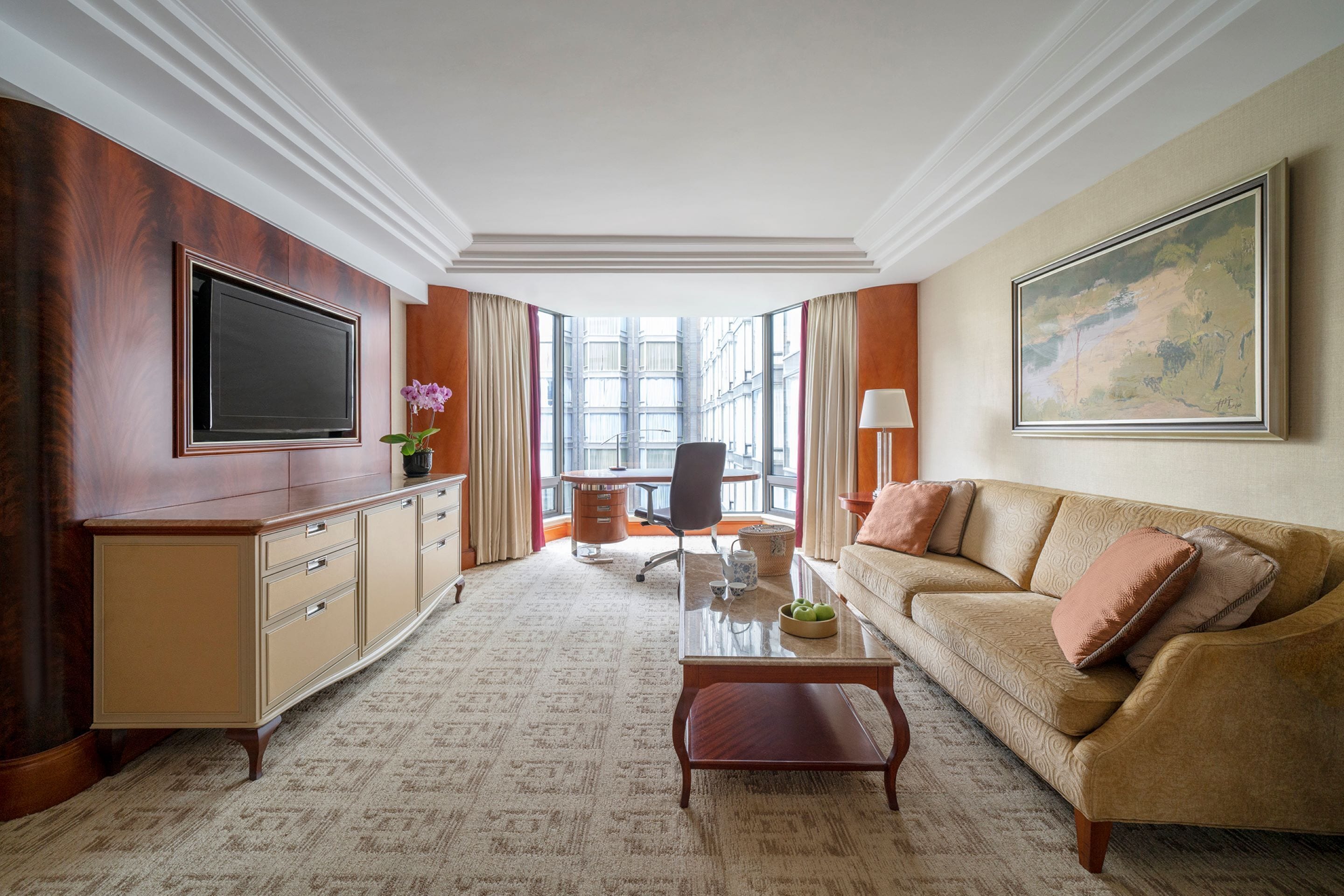 A spacious living room with a large flat-screen TV, a comfortable sofa, a coffee table, and a desk with a chair.
