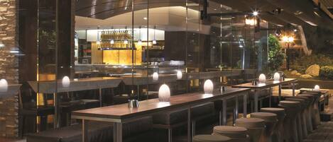 Un restaurant moderne doté d’un long comptoir, de tabourets et d’un espace bar visible à travers la paroi en verre.