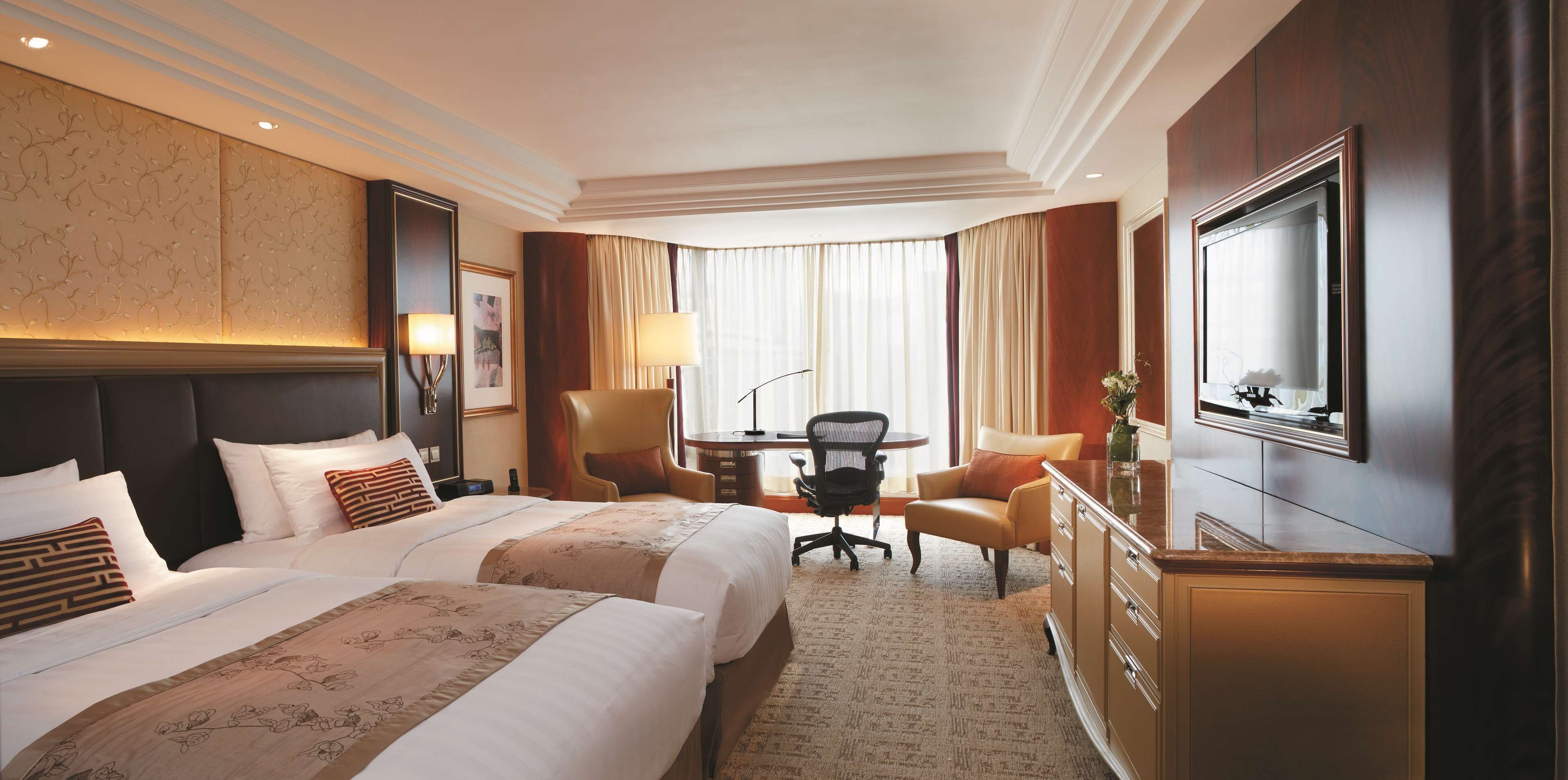 A hotel room with two beds, a desk, a chair, a television, and a large window with curtains.