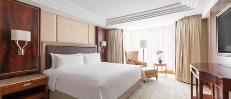 A hotel room with a large bed, bedside tables, a desk, and a television.