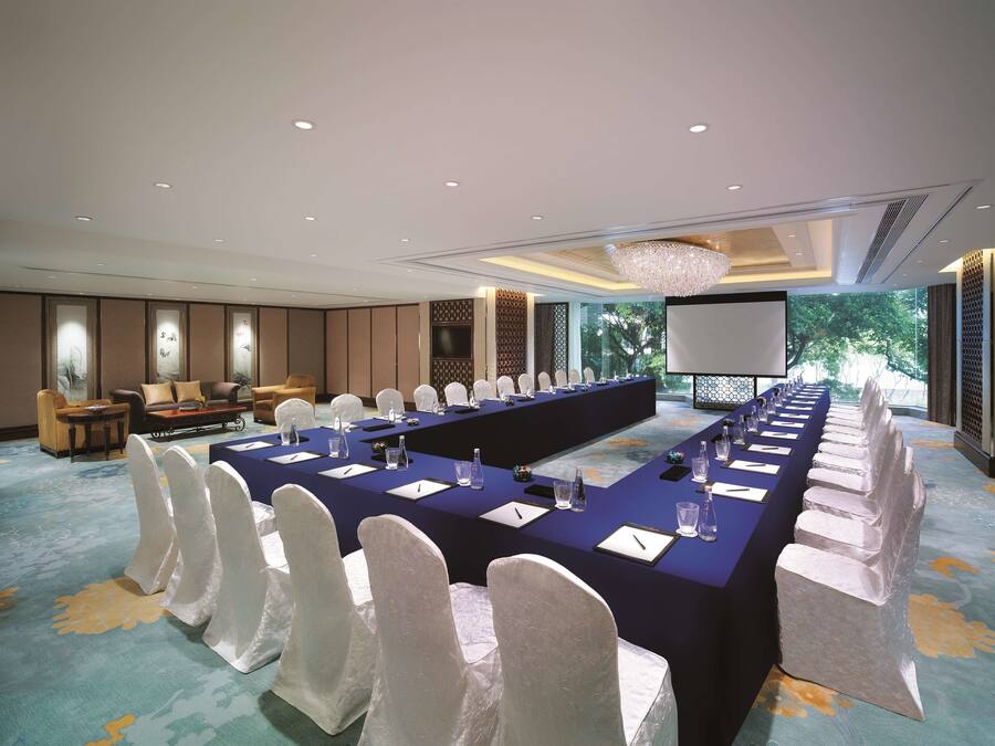A conference room with a long table, white chairs, and a large screen.