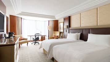 A hotel room with two large beds, a desk with a chair, a TV, and a window with curtains.