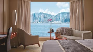 Habitación de hotel con cama, dos sillones, escritorio y vista a un horizonte urbano y al agua.