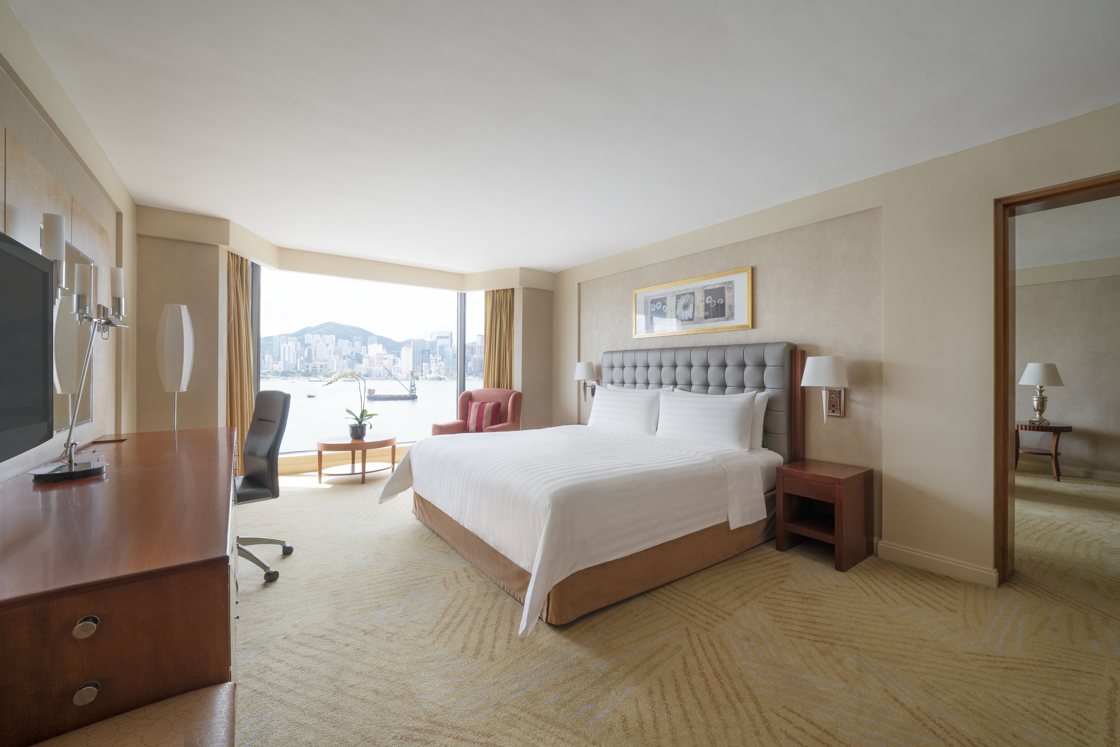 A hotel room with a large bed, a desk, a chair, a small table, and a view of a cityscape.