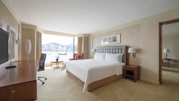 A hotel room with a large bed, a desk, a chair, a small table, and a view of a cityscape.