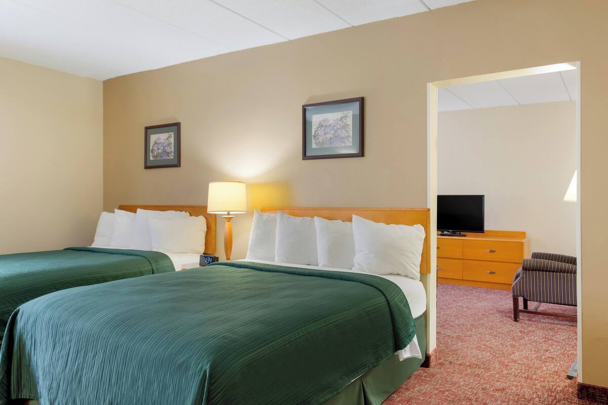 A hotel room with two beds, a television, a dresser, and two framed pictures on the wall.