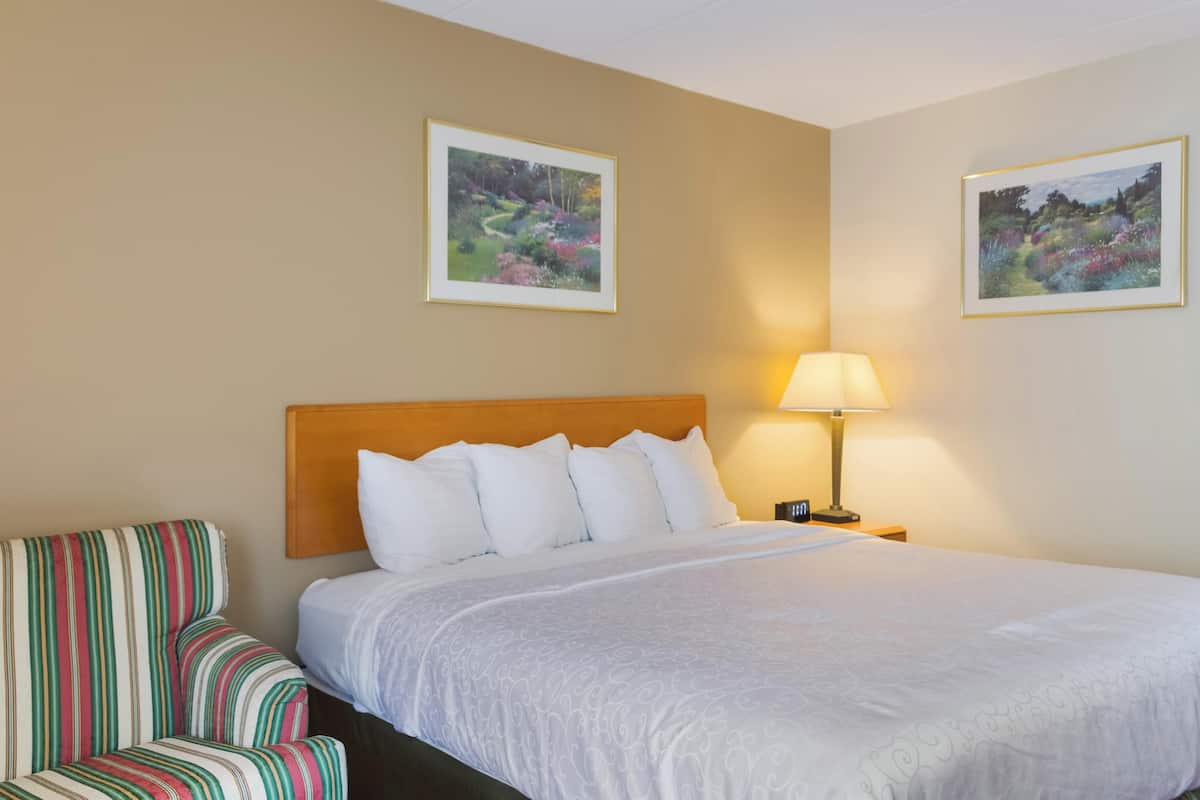 A hotel room with a large bed, a striped armchair, two wall-mounted lamps, and two framed pictures.