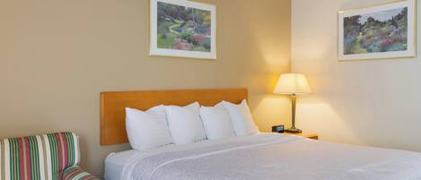 A hotel room with a large bed, a striped armchair, two wall-mounted lamps, and two framed pictures.
