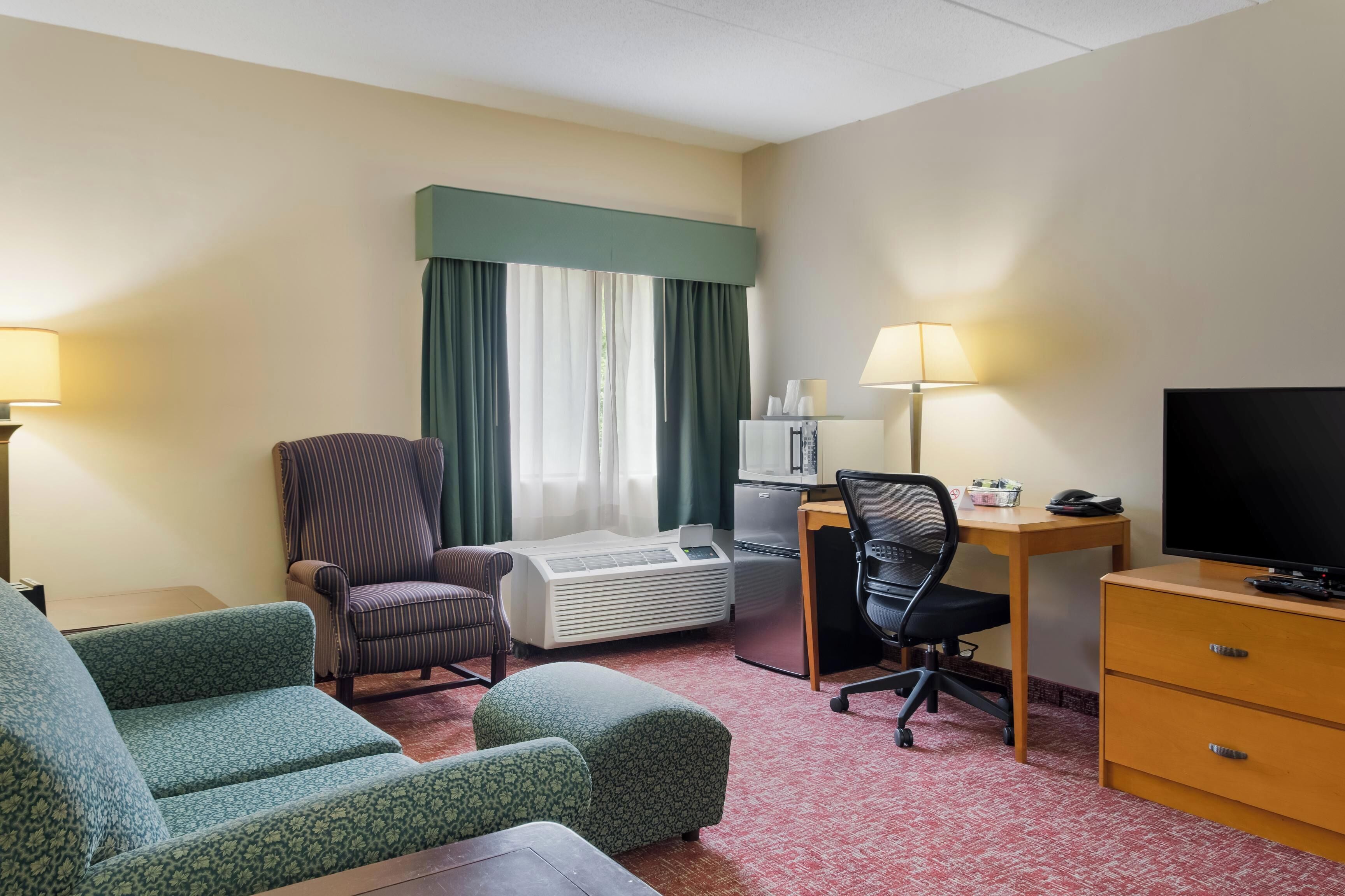 A hotel room with a bed, a desk with a computer, a chair, a TV, and a small kitchenette.
