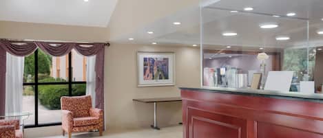 A reception area with a red counter, a framed painting on the wall, and a window with curtains.