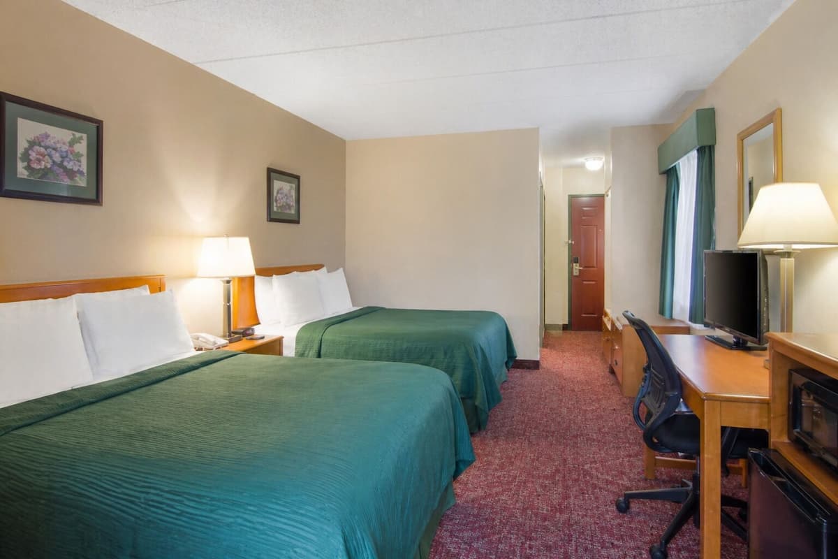 A hotel room with two beds, a desk with a computer, a chair, and a television.
