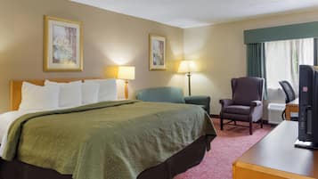 A hotel room with a large bed, two chairs, a desk, and a television.