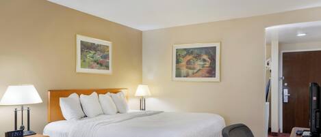 A hotel room with a bed, two bedside lamps, a desk with a computer, and two framed paintings on the wall.