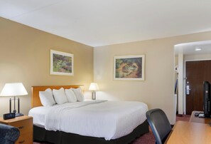 Een hotelkamer met een bed, twee bedlampen, een bureau met een computer, en twee ingelijste schilderijen aan de muur.