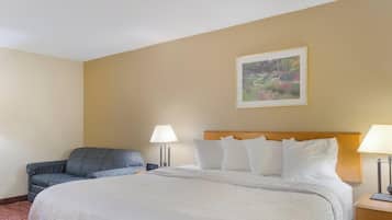 A hotel room with a large bed, two bedside lamps, a gray sofa, and a framed picture on the wall.