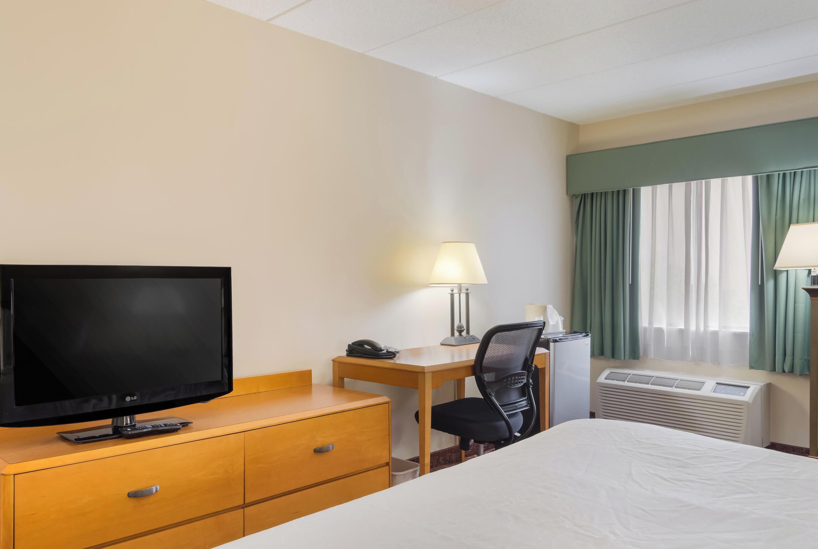 Habitación de hotel con cama, escritorio con lámpara, televisión, teléfono y aire acondicionado.