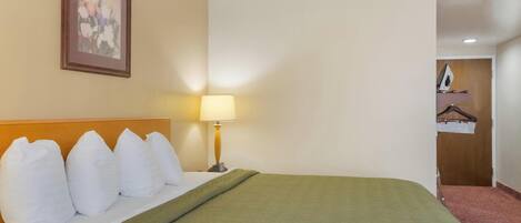 Ein Hotelzimmer mit einem Bett, einer Lampe, einem Bild an der Wand und einer Tür zu einem anderen Raum.