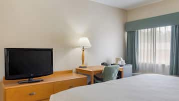 A hotel room with a bed, a TV, a desk with a lamp, a chair, and a window with curtains.