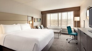 Habitación de hotel con una cama grande, un escritorio, una silla, un televisor, una lámpara y una ventana con cortinas.