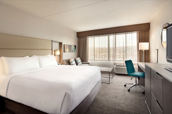 Une chambre d’hôtel avec un grand lit, un bureau, une chaise, une télévision, une lampe et une fenêtre avec des rideaux.