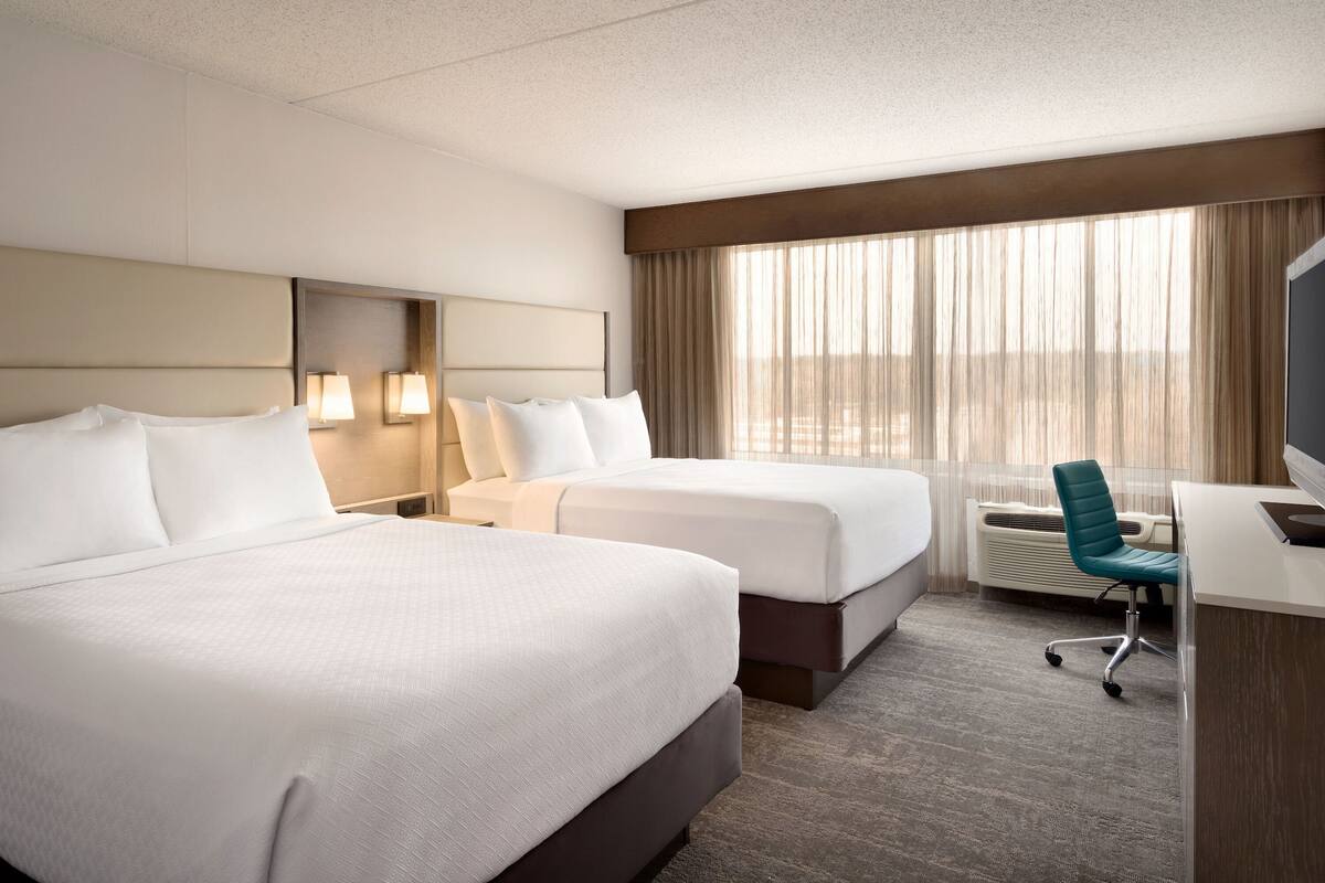 Une chambre d’hôtel avec deux lits, un bureau et une chaise.