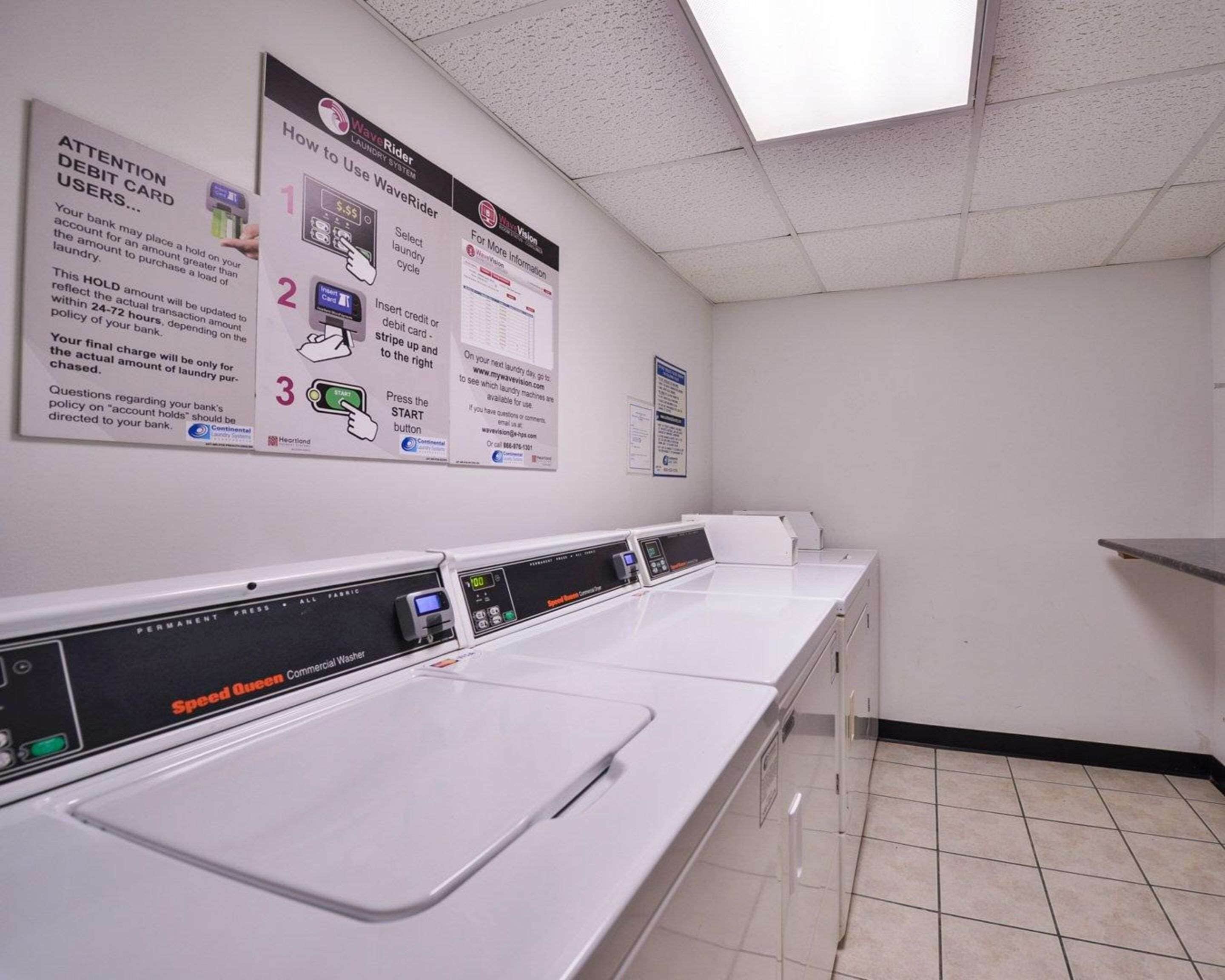 A laundry facility with multiple washing machines, a control panel, and instructional posters on the wall.