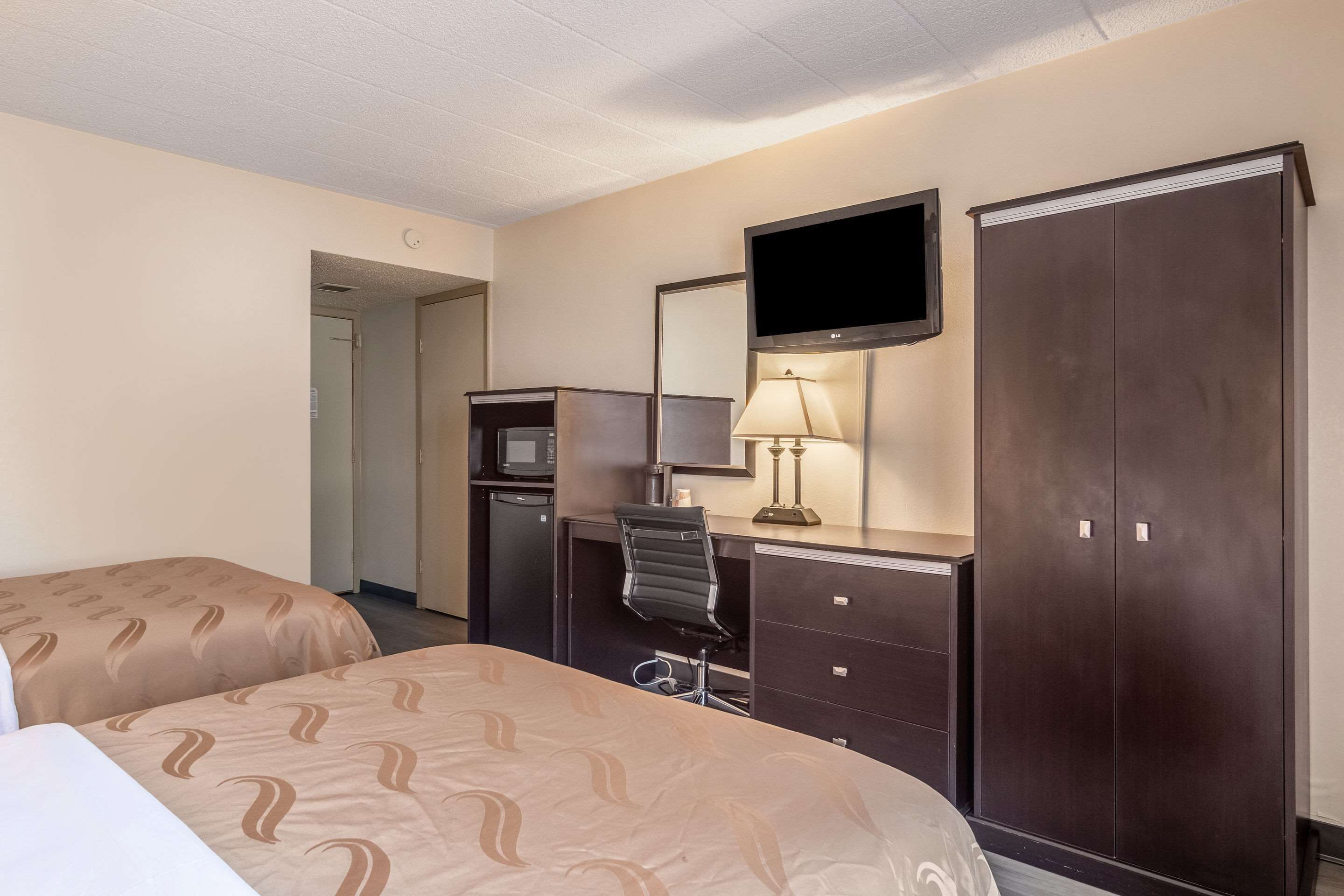 A hotel room with a bed, desk, chair, TV, wardrobe, and a lamp.