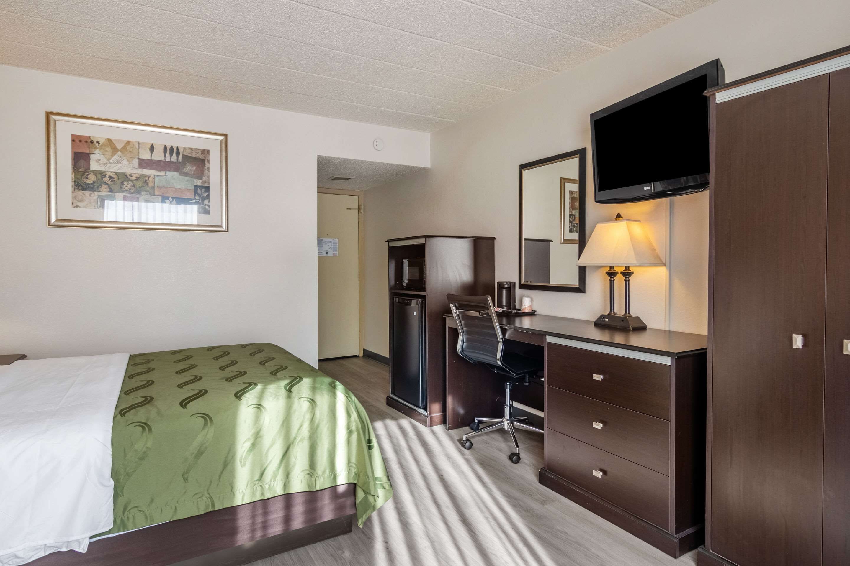 A hotel room with a bed, a desk, a chair, a television, and a wardrobe.
