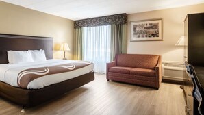 A hotel room with a large bed, a sofa, a television, and a window with curtains. - Quality Inn & Suites Indiana South (Indiana)