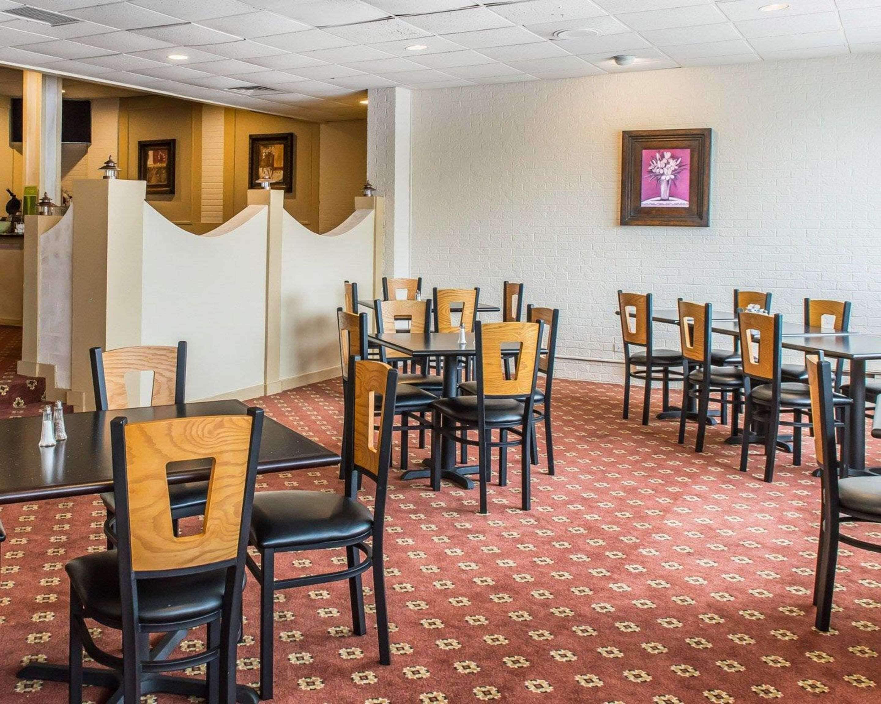 A hotel dining area with multiple tables and chairs, a patterned carpet, and a framed picture on the wall.