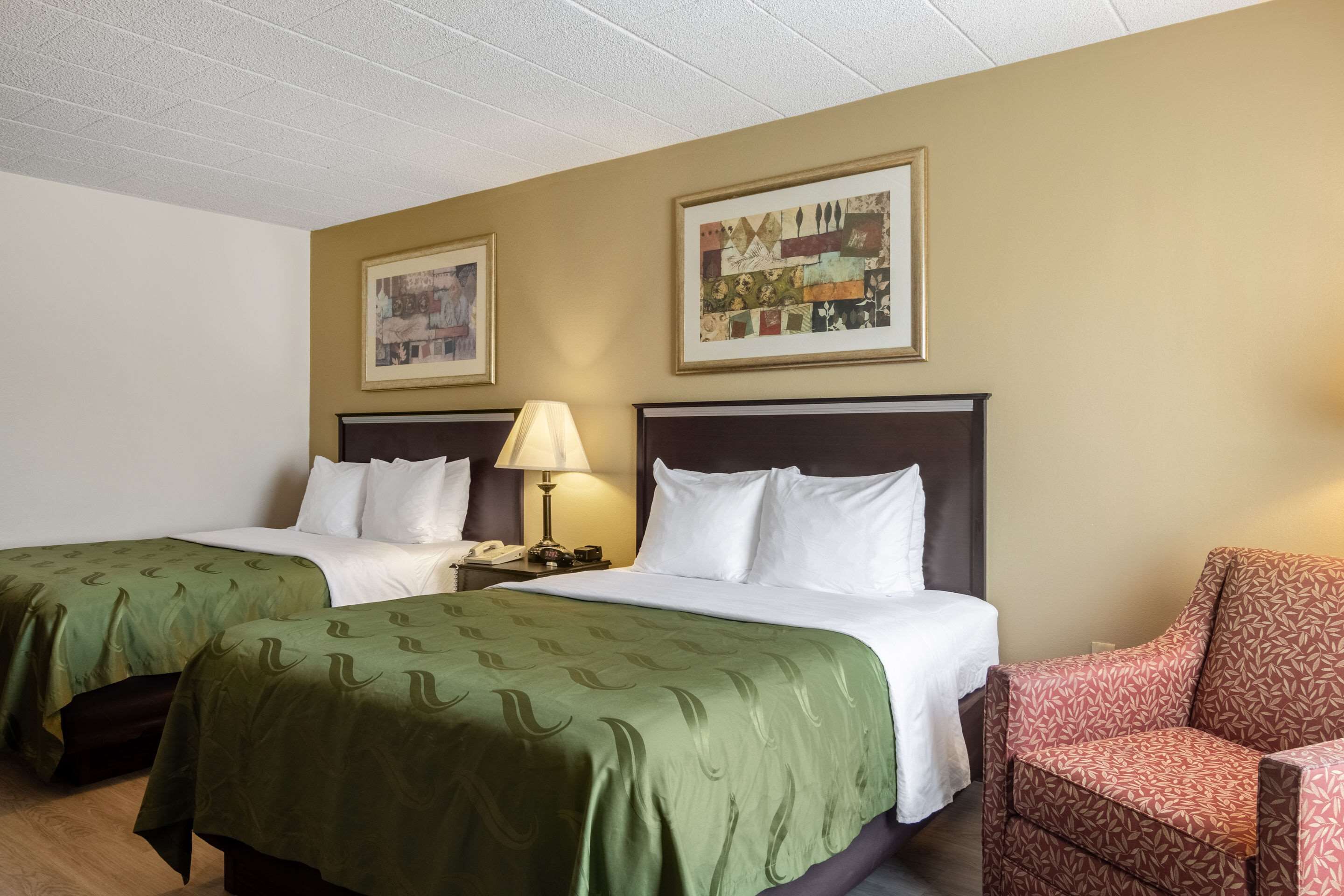 A hotel room with two beds, a chair, and two framed pictures on the wall.