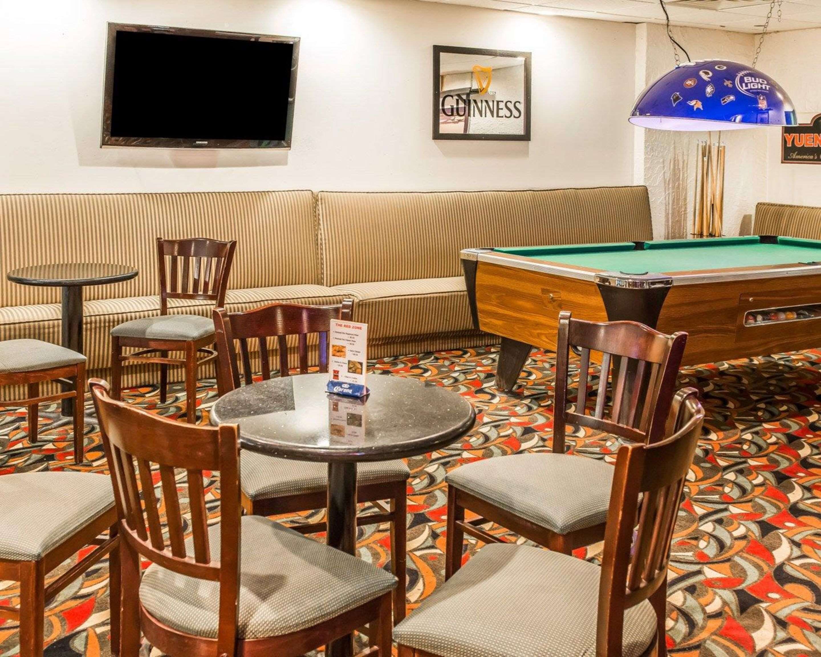 Uma sala de bilhar com mesa de sinuca, cadeiras, uma televisão e churrasqueira com a marca Bud Light.