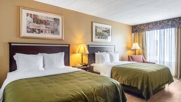 Habitación de hotel con dos camas, cada una con colcha verde, cabecero de madera y ropa de cama blanca. Se observan dos mesitas de noche con lámparas, un cuadro enmarcado en la pared y una ventana con cortinas.