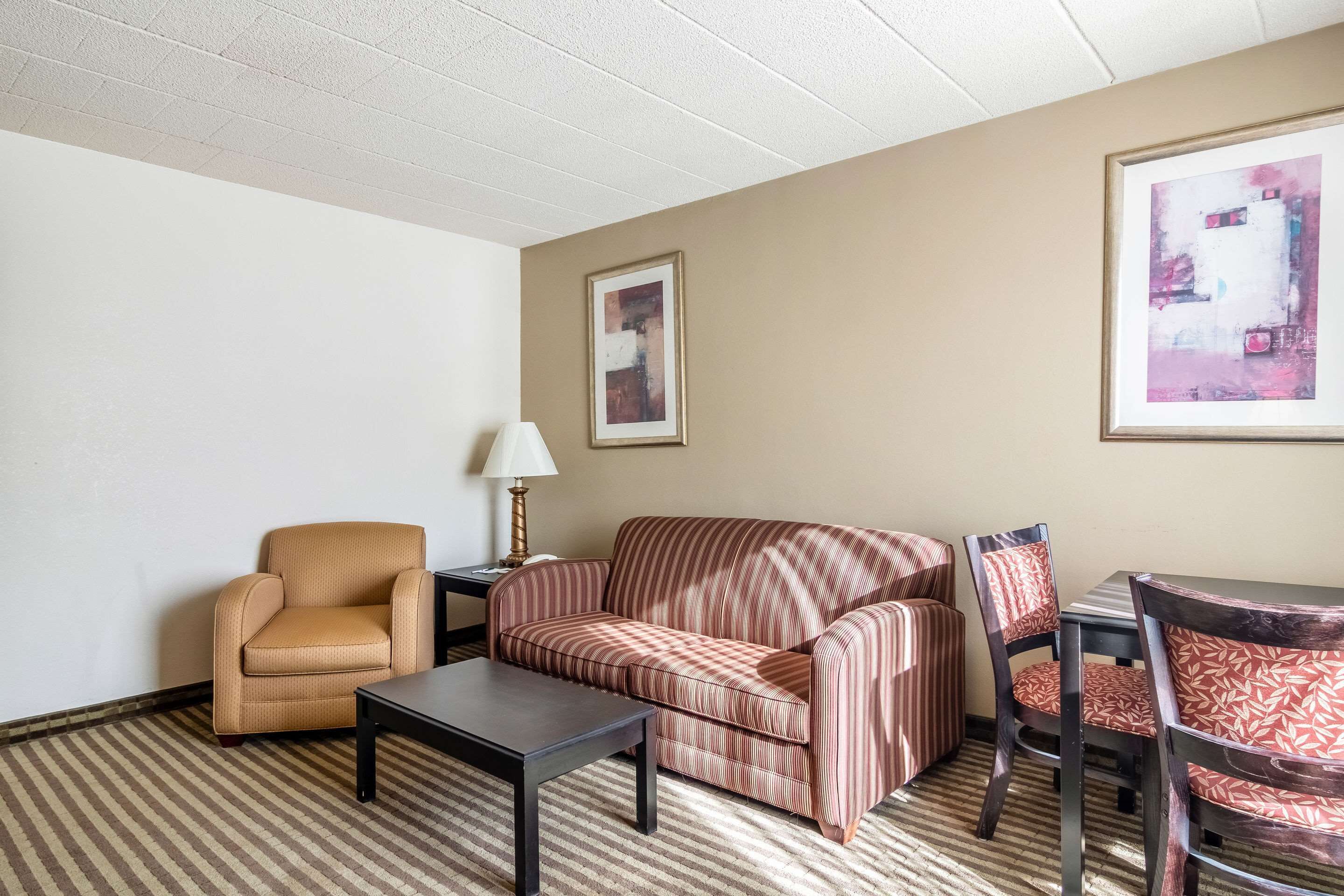 Habitación de hotel con un sofá a rayas, un sillón individual, una mesita y un cuadro abstracto enmarcado en la pared.