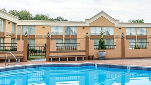 A swimming pool with a tiled edge, surrounded by a building with large windows and a flat roof. - Quality Inn & Suites Indiana South (Indiana)