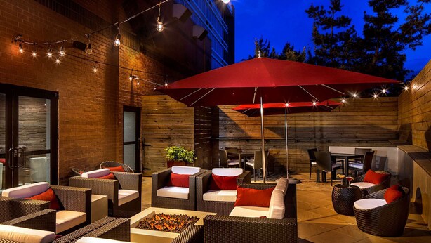 An outdoor patio area with wicker furniture, red umbrellas, and string lights. - DoubleTree by Hilton Hotel Largo/Washington DC (Upper Marlboro)
