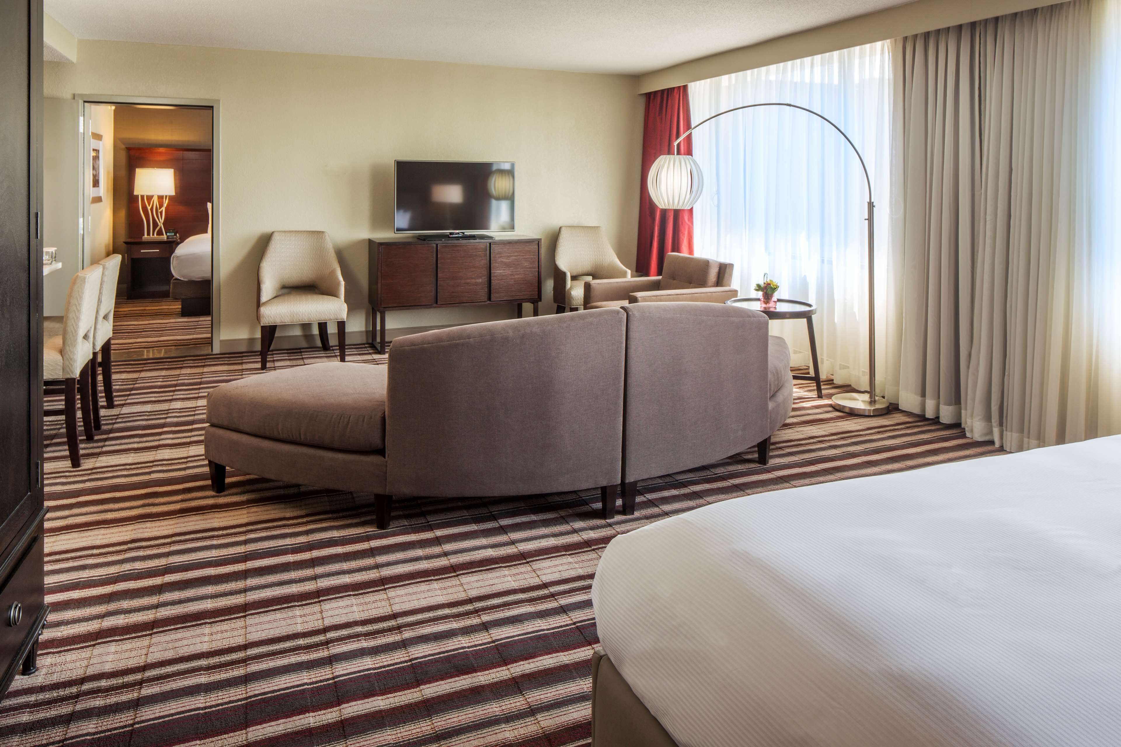 A hotel room with a large bed, a sofa, a TV, and a desk with a lamp.