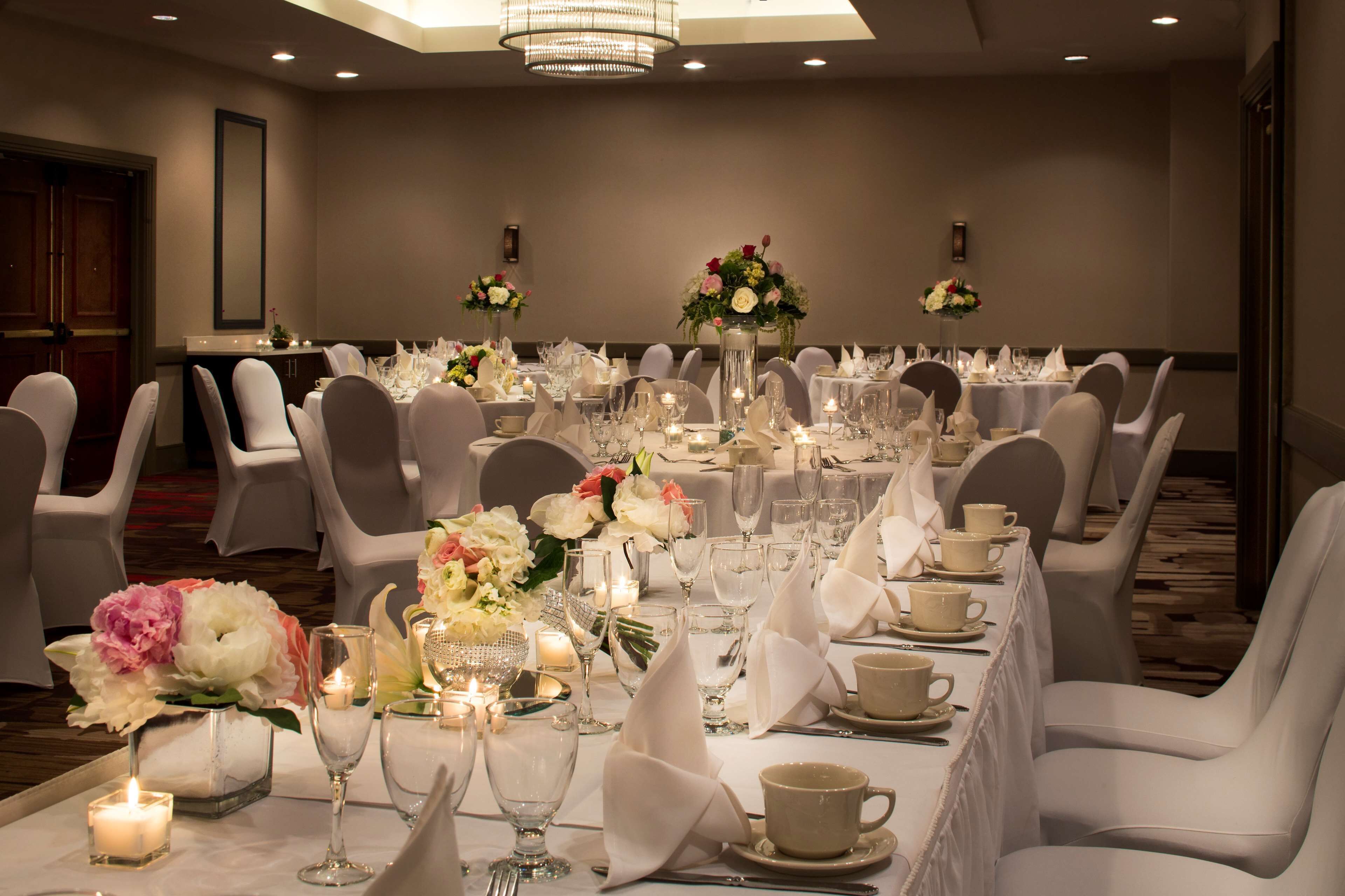 A banquet hall with round tables set for a formal event, featuring white tablecloths, candles, and floral centerpieces.