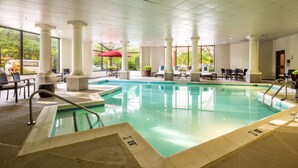 An indoor swimming pool with clear water, surrounded by white columns and a sunlit area with chairs and tables. - DoubleTree by Hilton Hotel Largo/Washington DC (Upper Marlboro)