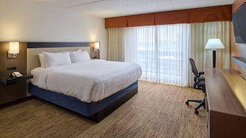 Une chambre d’hôtel avec un grand lit, un bureau avec une chaise, une télévision et un téléphone sur la table de chevet.