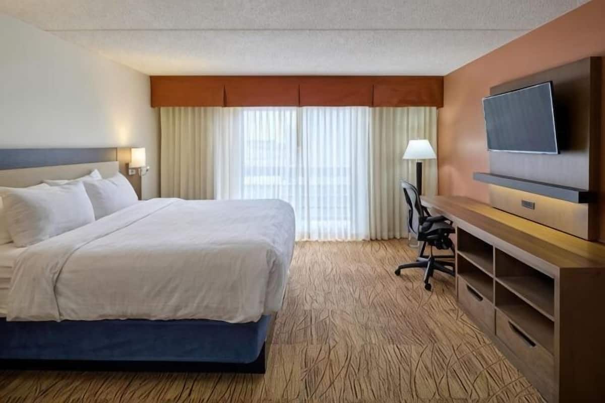 A hotel room with a bed, a desk with a chair, a television, and a window with curtains.