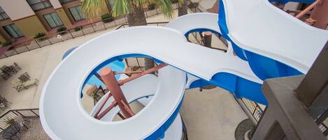 A multi-level water slide structure with blue and white colors, surrounded by outdoor seating and palm trees.