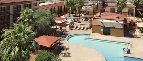 A resort with a large swimming pool, palm trees, and a view of distant mountains.