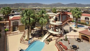 Un resort con parque acuático, que incluye piscina, palmeras y vistas a montañas y un aeropuerto al fondo.