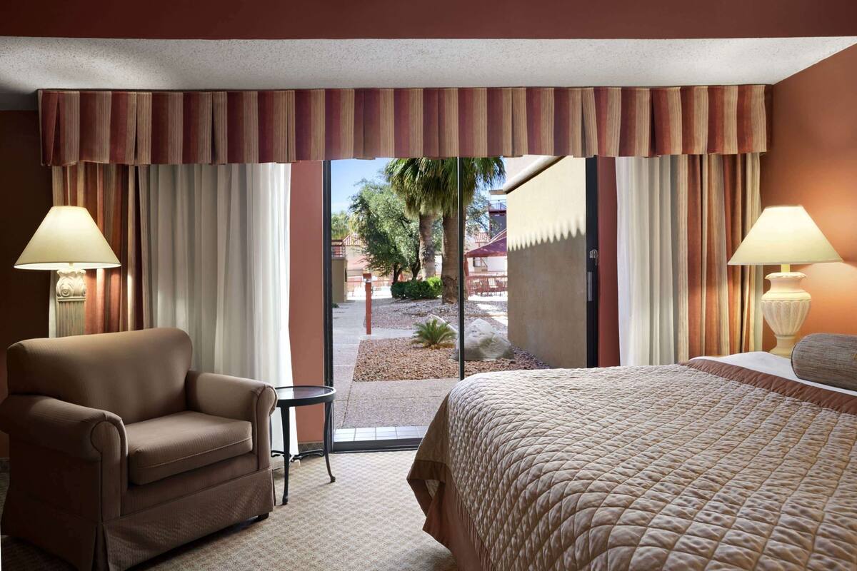 A hotel room with a bed, a chair, a table, and a view of the outside.