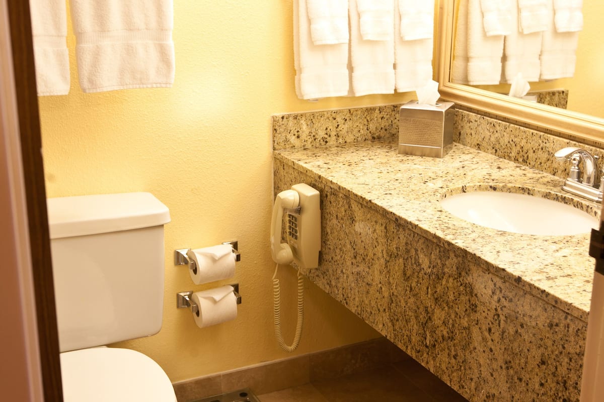 A bathroom with a toilet, sink, and mirror. There are towels hanging on the wall and a trash can.