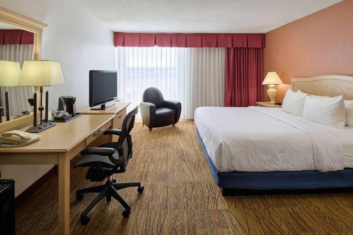 A hotel room with a bed, desk, chair, television, and a window with curtains.