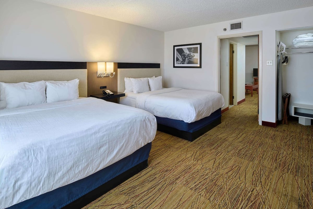 A hotel room with two beds, a nightstand, a wall-mounted lamp, a framed picture, and a walk-in closet.