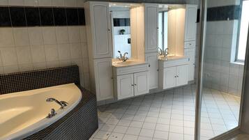 A modern bathroom with a large bathtub, two sinks, and a shower area.