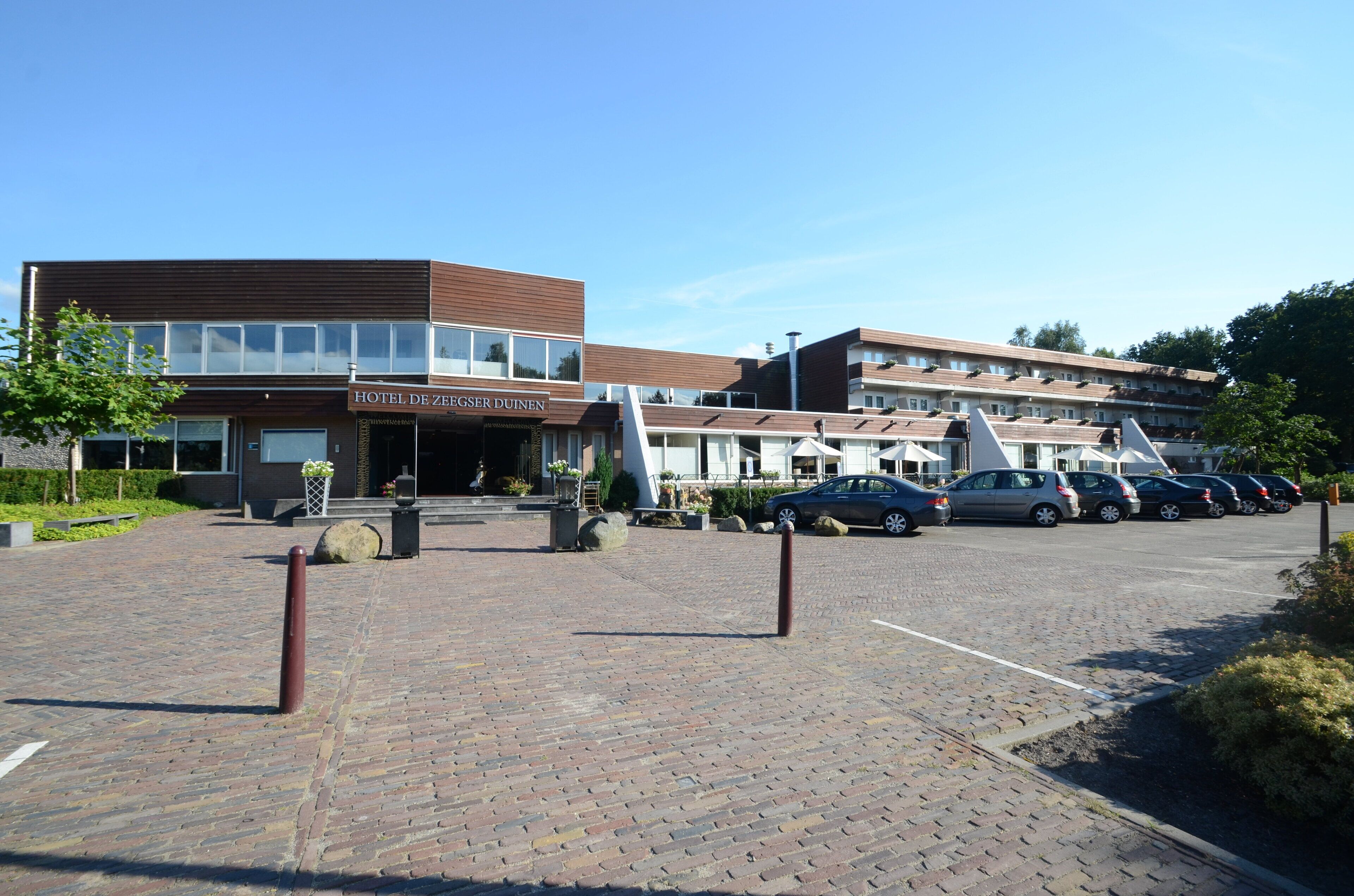 A hotel with a modern design, featuring a prominent entrance and a parking area with several cars.